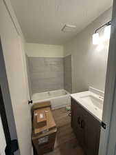 Bathroom with tiled shower / bath, wood-type flooring, vanity, and a textured ceiling