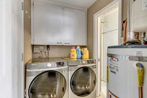 Washroom with cabinets, independent washer and dryer, light tile patterned floors, and secured water heater