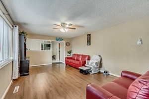 Living room with wood-type flooring, a wood stove, a textured ceiling, and ceiling fan