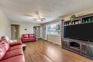 Living room featuring ceiling fan, wood-type flooring, and a textured ceiling