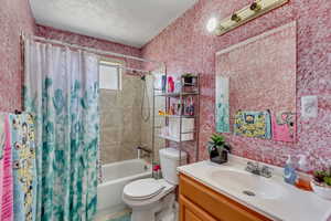 Full bathroom with vanity, a textured ceiling, toilet, and shower / bath combo