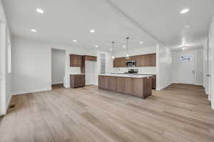 Kitchen featuring stainless steel appliances, hanging light fixtures, a kitchen island with sink, and light wood-type flooring