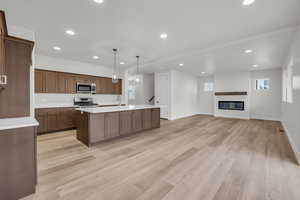 Kitchen featuring pendant lighting, appliances with stainless steel finishes, light hardwood / wood-style flooring, and a center island with sink