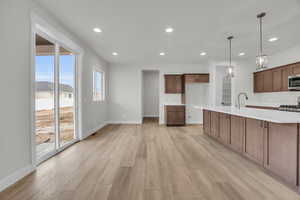 Kitchen featuring sink, appliances with stainless steel finishes, a kitchen island with sink, hanging light fixtures, and light hardwood / wood-style floors