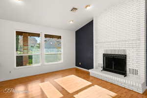 Unfurnished living room with lofted ceiling, a brick fireplace, and hardwood / wood-style flooring