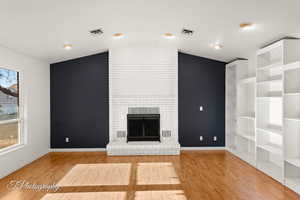 Unfurnished living room featuring hardwood / wood-style flooring, vaulted ceiling, and a brick fireplace