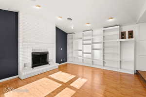 Unfurnished living room featuring hardwood / wood-style flooring, vaulted ceiling, and a fireplace