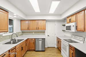 Kitchen featuring sink, backsplash, white appliances, and light wood-type flooring