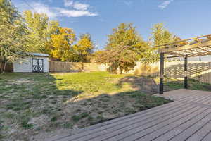 View of yard with a wooden deck, a storage unit, and a pergola