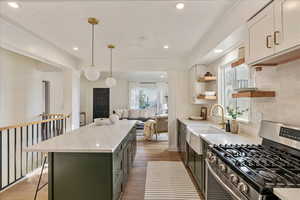 Kitchen with pendant lighting, a center island, stainless steel gas range oven, light stone countertops, and white cabinets