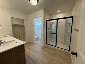 Full bath with toilet, a stall shower, a sink, wood finished floors, and baseboards