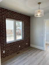 Unfurnished dining area with brick wall, a textured ceiling, and light hardwood / wood-style flooring