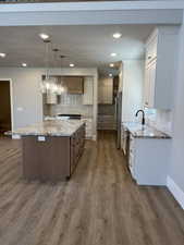 Kitchen featuring appliances with stainless steel finishes, hanging light fixtures, dark hardwood / wood-style floors, a center island, and light stone countertops