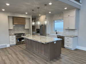 Kitchen featuring white cabinetry, a spacious island, premium appliances, decorative light fixtures, and custom exhaust hood