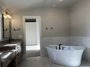 Bathroom with vanity, a bathing tub, vaulted ceiling, and tile walls