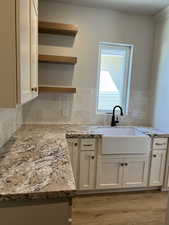 Kitchen with white cabinetry, sink, backsplash, light stone counters, and light hardwood / wood-style flooring