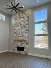 Unfurnished living room featuring a stone fireplace, wood-type flooring, and ceiling fan