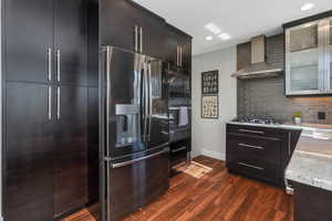 Kitchen featuring dark hardwood / wood-style floors, backsplash, light stone counters, black appliances, and wall chimney range hood