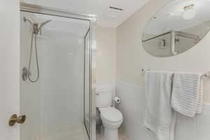 Bathroom with toilet, tile patterned flooring, a shower with door, and tile walls