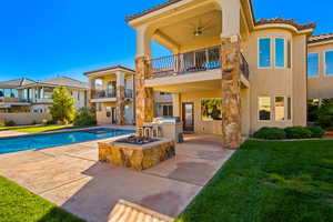 Rear view of property featuring a fenced in pool, ceiling fan, a yard, a balcony, and exterior kitchen