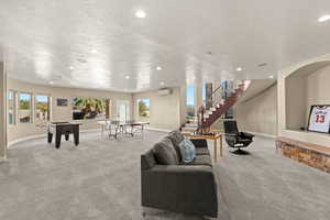 Living room featuring a wall mounted AC, light carpet, and a textured ceiling