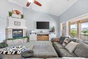 Carpeted living room featuring lofted ceiling, a brick fireplace, ornamental molding, and ceiling fan