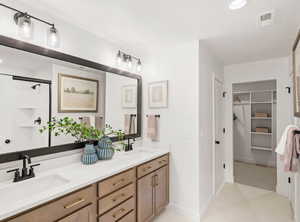 Full bath with double vanity, a spacious closet, visible vents, and a sink