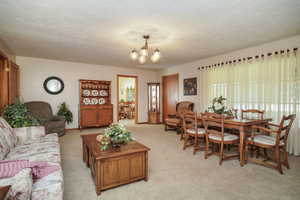 Living room featuring an inviting chandelier, light carpet, and a textured ceiling