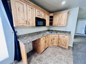 Kitchen featuring dark stone counters, light brown cabinetry, sink, and a textured ceiling