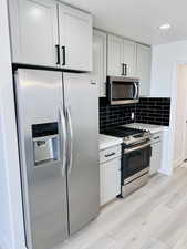 Kitchen featuring decorative backsplash, stainless steel appliances, and white cabinets