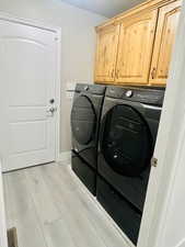 Clothes washing area with light hardwood / wood-style flooring, cabinets, and washing machine and clothes dryer