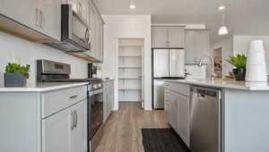 Kitchen featuring gray cabinets, appliances with stainless steel finishes, hanging light fixtures, hardwood / wood-style floors, and a textured ceiling