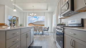 Kitchen with stainless steel appliances, gray cabinets, pendant lighting, and a tray ceiling