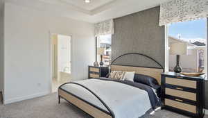 Bedroom with multiple windows, a tray ceiling, light colored carpet, and ensuite bathroom