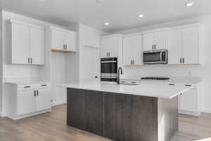 Kitchen featuring appliances with stainless steel finishes, sink, white cabinets, a kitchen island with sink, and light hardwood / wood-style floors