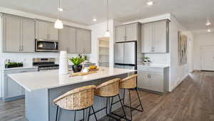 Kitchen featuring stainless steel appliances, hanging light fixtures, gray cabinetry, and a kitchen bar