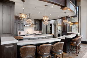 Kitchen with tasteful backsplash, hanging light fixtures, an island with sink, and dark brown cabinets