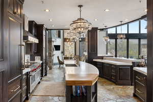 Kitchen featuring dark brown cabinetry, hanging light fixtures, an inviting chandelier, and wall chimney exhaust hood