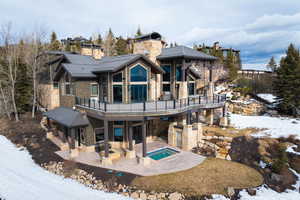 Snow covered back of property featuring a jacuzzi and a patio