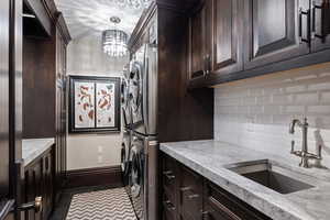 Laundry room with sink, tile patterned flooring, cabinets, stacked washer and clothes dryer, and a chandelier