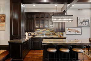 Bar with decorative backsplash, dark hardwood / wood-style flooring, light stone countertops, and dark brown cabinets