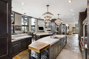 Kitchen with decorative light fixtures, a chandelier, an island with sink, and dark brown cabinets