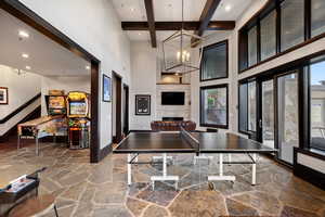 Playroom featuring beam ceiling, a fireplace, a chandelier, and a high ceiling