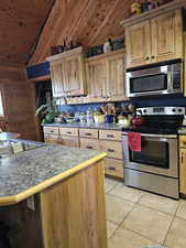 Kitchen featuring light tile patterned floors, sink, wooden walls, stainless steel appliances, and wooden ceiling