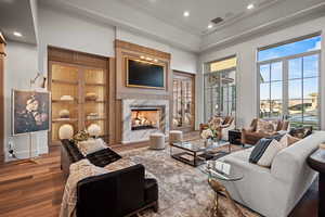 Living room featuring hardwood / wood-style flooring, crown molding, a towering ceiling, and a fireplace