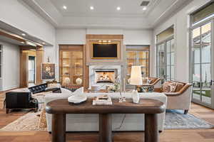 Living room with a towering ceiling, ornamental molding, a raised ceiling, a premium fireplace, and light wood-type flooring