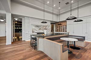 Kitchen with a high ceiling, white cabinetry, hardwood / wood-style floors, and pendant lighting