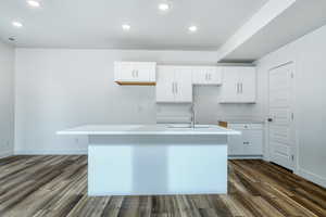 Kitchen with sink, dark hardwood / wood-style flooring, an island with sink, and white cabinets