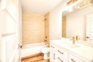 Full bathroom featuring hardwood / wood-style flooring, tiled shower / bath, vanity, and toilet