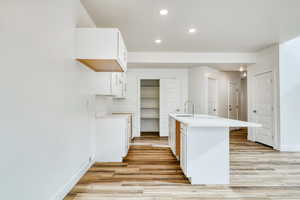 Kitchen with white cabinetry, sink, a center island with sink, and light wood-type flooring